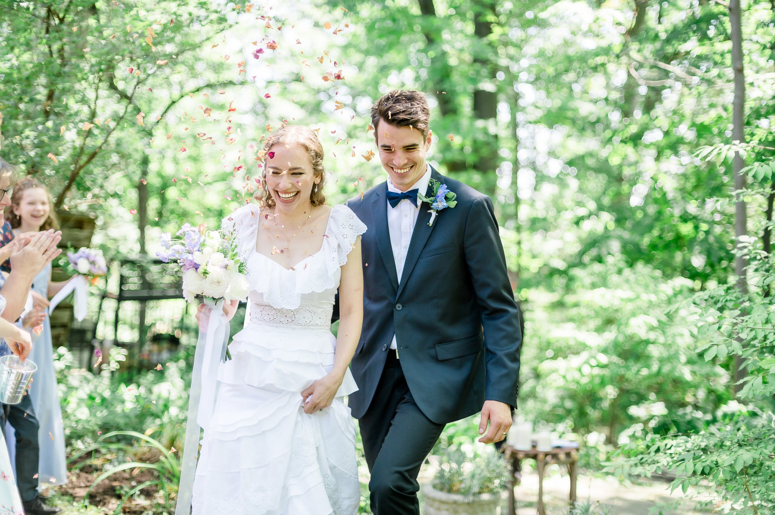 bride and groom walk through the flower petals being thrown over  them.