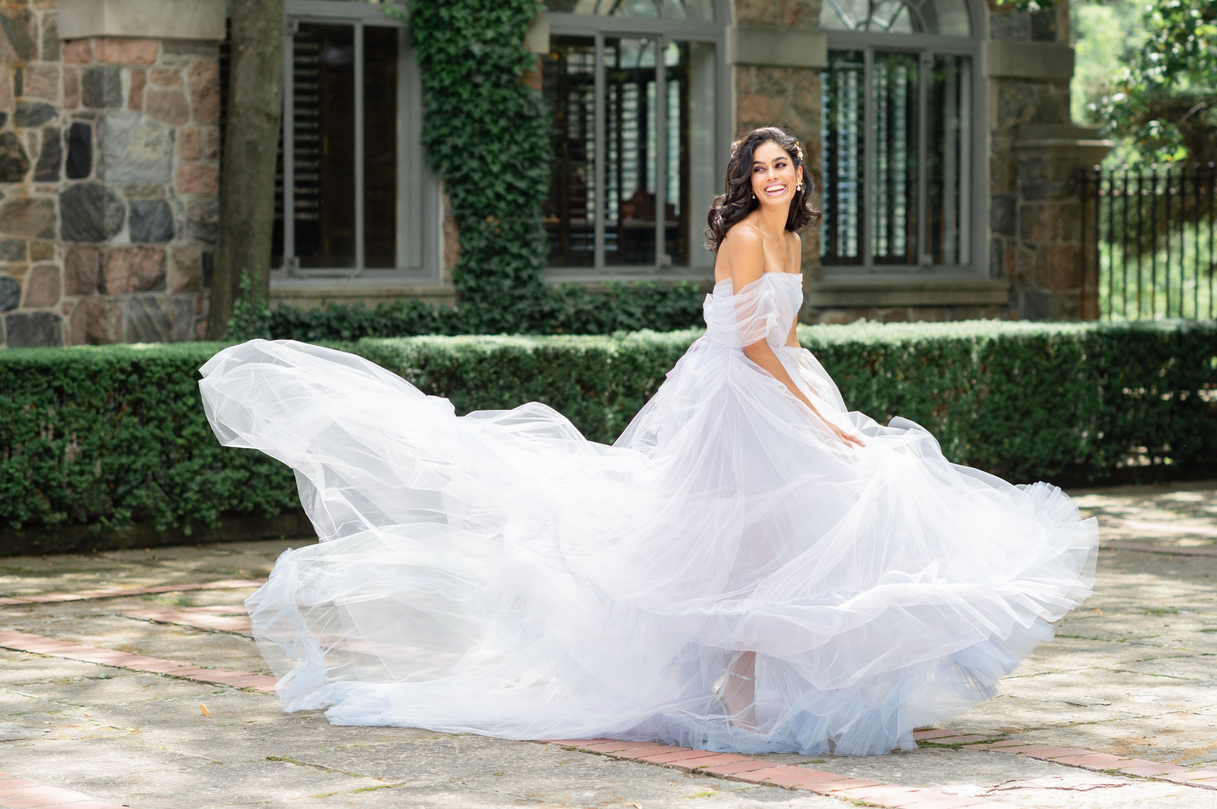 brunette model seen smiling wide and spinning in a lilac tulle dress in the fron garden of Graydon hall Manor