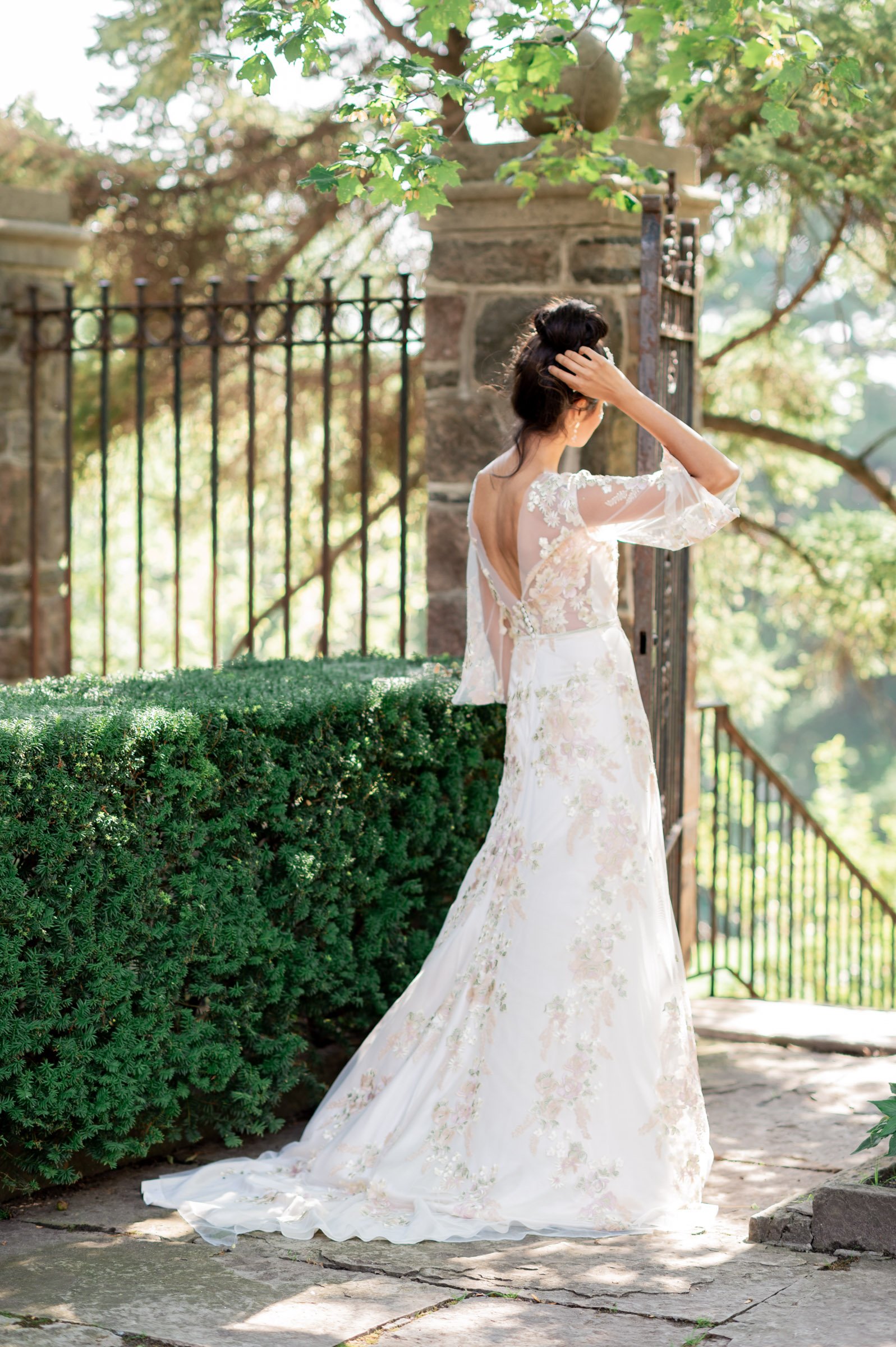 indian looking model wearing silk and floral lace appliquee dress, seen from the back- one hand up on her hair with a bun in it.