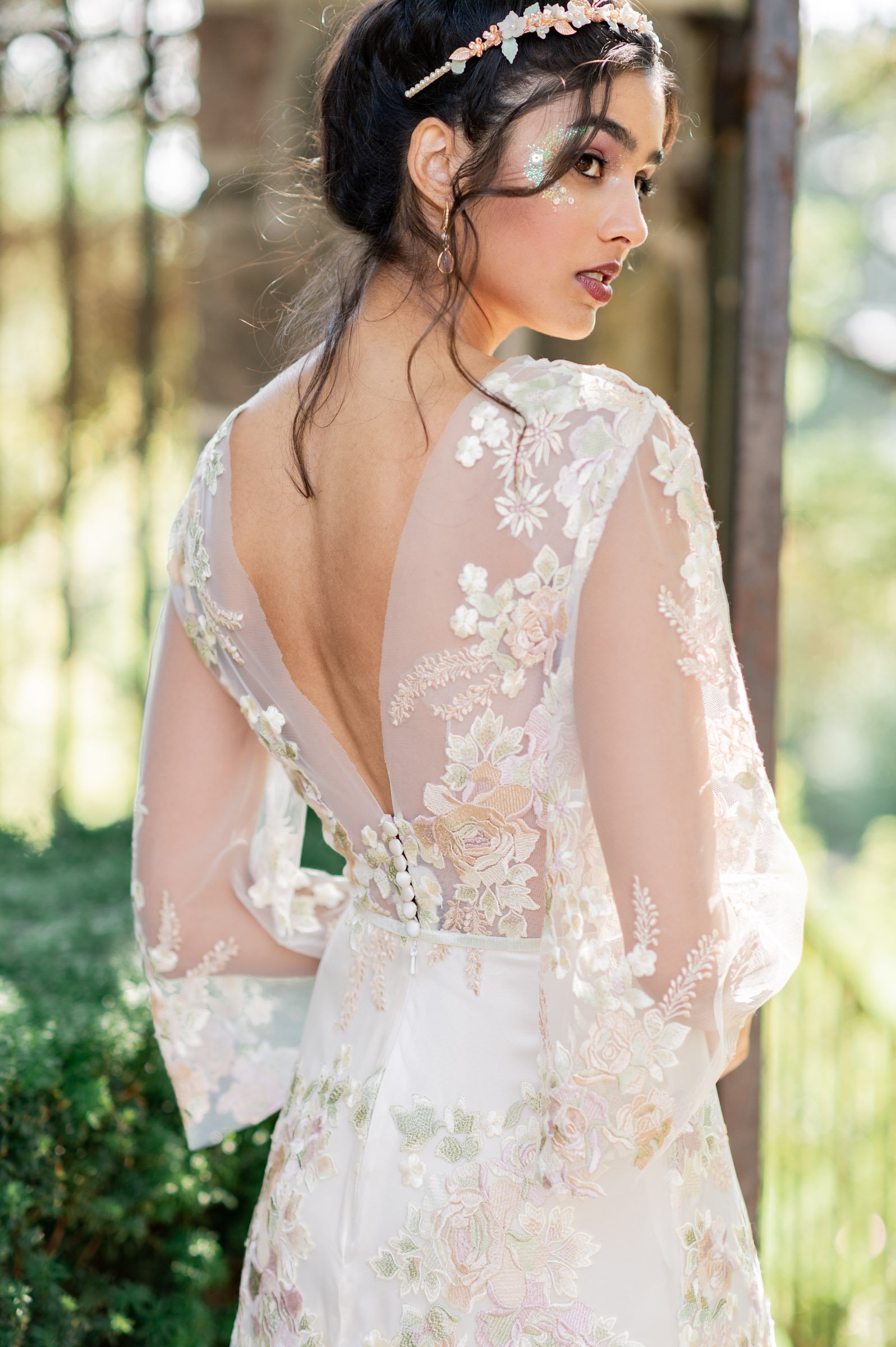 Beautiful indian looking model looks over her shoulder wearing a tiara and shimmery makeup with a dark lip with a lace appliquee dress over silk in front of Graydon Hall Manor at the gate. sun is shining bright!