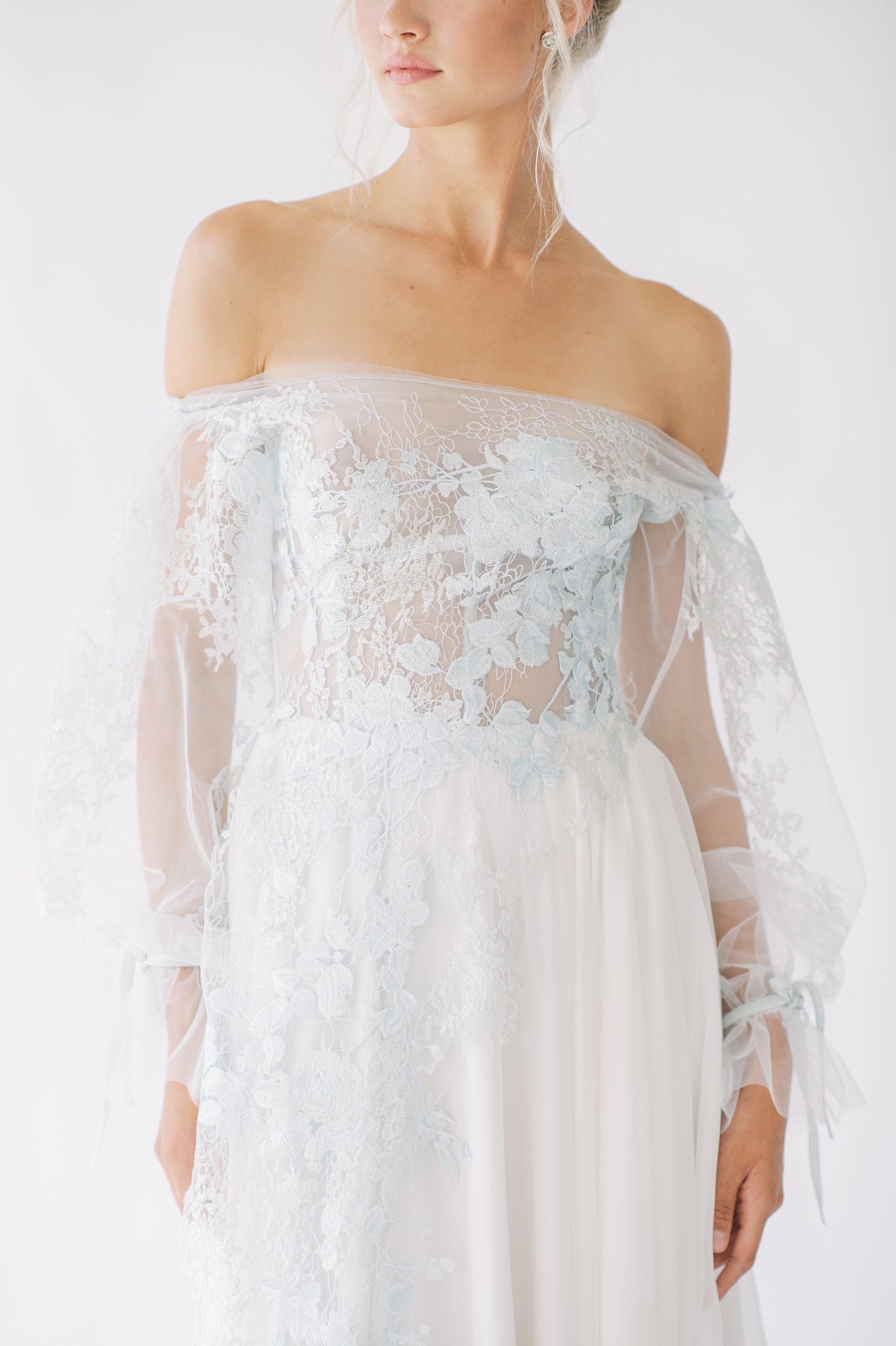 light blue lace applique with sleeves in organza over a silky white skirt. blonde model only lower half of face and decolleteage is visible.