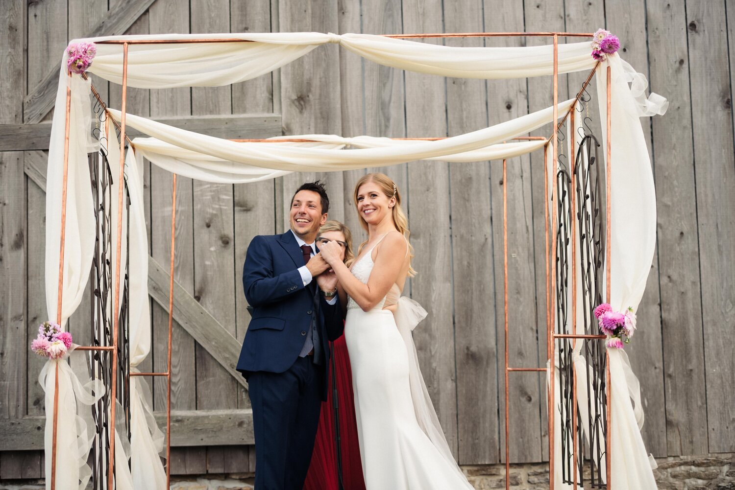 The bride and groom holding hands under the Chuppah on their wedding day at the Old Third in Prince Edward County.