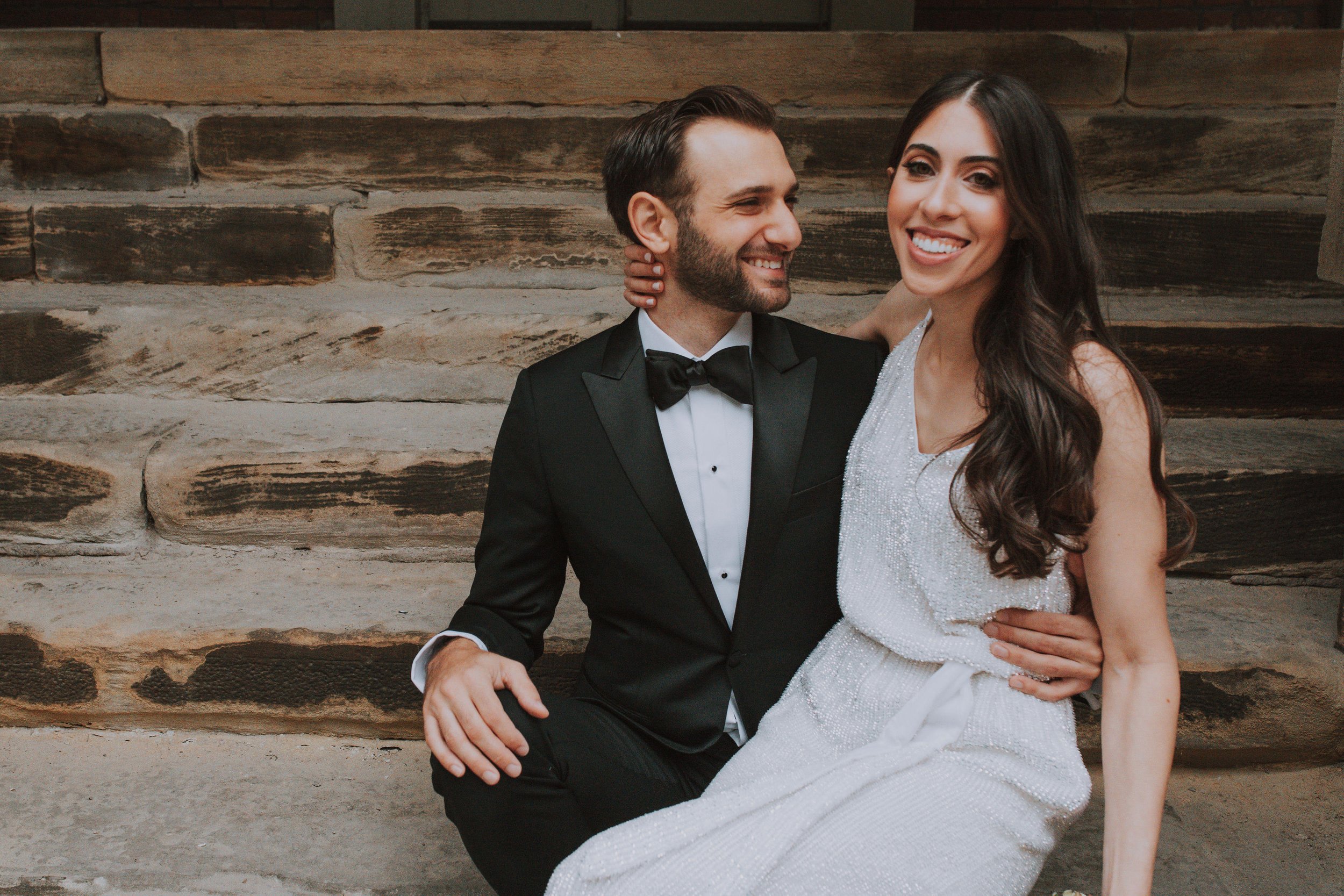 bride and groom sit together on the steps of an old building.